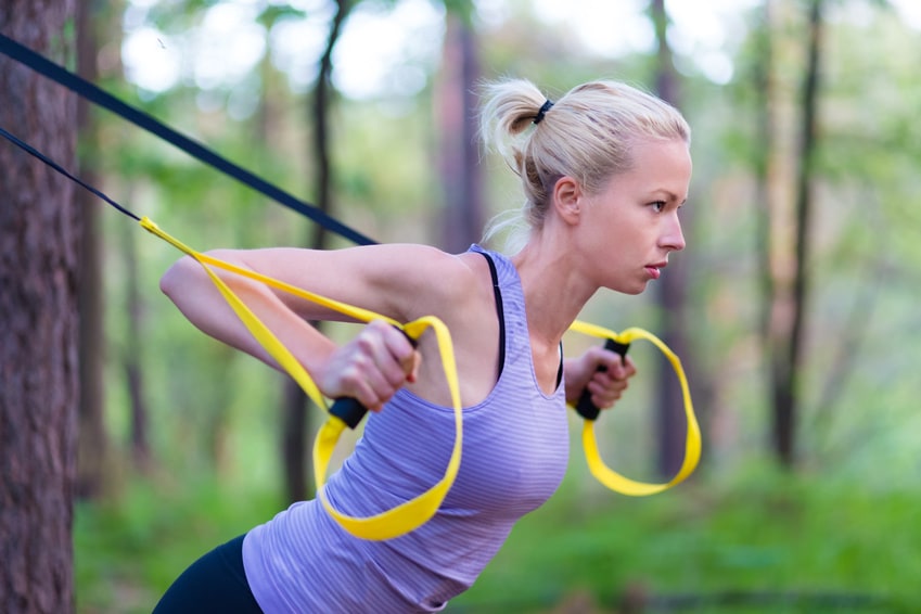 Frau, die mit zwei Fitnessbändern im Wald trainiert